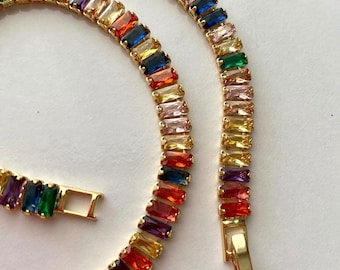 May include: A gold chain necklace with a rainbow of colorful rectangular stones. The necklace has a clasp closure.