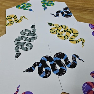 May include: A set of six hexagonal cards with colorful snake illustrations. Each card features a different snake design with various patterns and colors, including black, blue, green, yellow, pink, and purple.