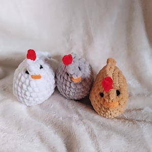 May include: Three crocheted chicken plushies. One is white, one is gray, and one is brown. Each has a red comb and a yellow beak.