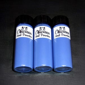 May include: Three blue bottles of "Obscurios Anil Powder" with black caps and white labels featuring a panda logo. The bottles are filled with a vibrant blue powder, set against a dark background.