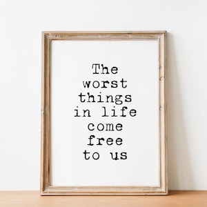 Puede incluir: Una impresión enmarcada con la cita, "Las peores cosas de la vida son gratis", en una fuente de máquina de escribir. El marco es de color marrón claro y el fondo es blanco.