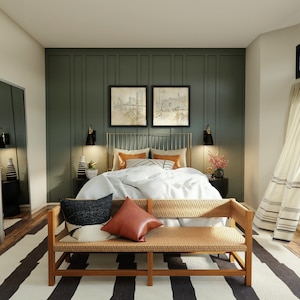 May include: A bedroom with a green wall and a bed with a white duvet and a woven bench at the foot of the bed. The bed has a gold metal frame and a white and black patterned throw pillow.