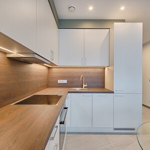May include: A modern kitchen with white cabinets, a wood worktop, and a stainless steel sink. The kitchen has a wood backsplash with under-cabinet lighting.