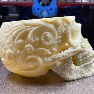 May include: A white skull planter with intricate floral designs. The skull is made of a smooth, white material and has a detailed, ornate design.