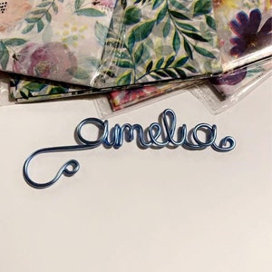Könnte beinhalten: Ein blaues Draht-Namenschild mit der Aufschrift "Amelia".