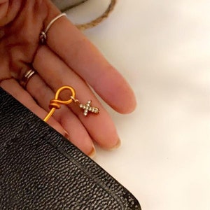 May include: A gold-colored bookmark with a small, sparkly cross charm. The bookmark is tucked into the corner of a black leather-bound book.