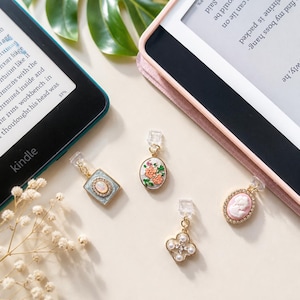 May include: Four decorative page markers with gold-tone metal clips and dangling charms. One charm is a square light blue frame with an oval centre, one is an oval with orange flowers, one is a pink cameo, and one is a four-leaf clover with pearls.