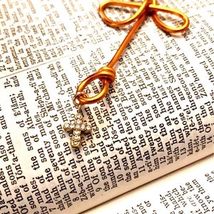 May include: A gold wire bookmark shaped like the word "love" is placed on an open Bible. The bookmark is adorned with a small, sparkling, diamond-encrusted cross.
