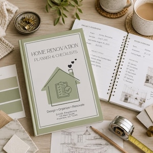 May include: A home renovation planner and checklist book with a green cover, open to show interior pages. The book is surrounded by design elements like paint swatches, a measuring tape, and a pencil. A cup of coffee and a notebook are also visible.