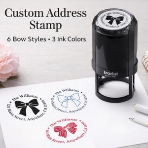 May include: A black Trodat Printy 4642 self-inking custom address stamp with a circular impression area. The stamp features a bow graphic and the text "the Williams, 123 Main Street, Anywhere, CA 12345" in black, blue, and red ink on white paper.