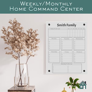 May include: A white acrylic Weekly/Monthly Home Command Center with the text "Smith Family". The board includes sections for daily and monthly to-do lists, and a weekly calendar. A vase with dried flowers is on the left.