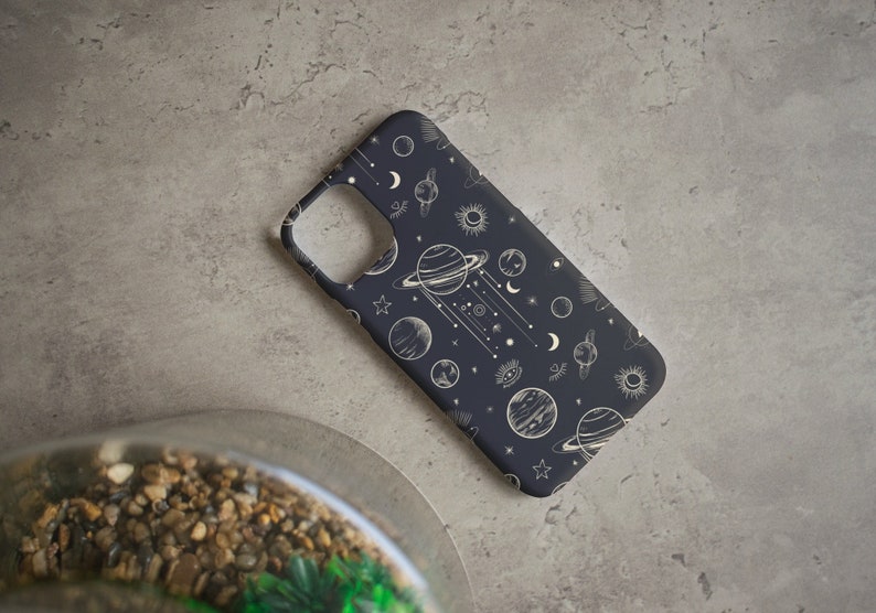 Peut inclure: Une coque de t&eacute;l&eacute;phone noire avec un motif c&eacute;leste blanc repr&eacute;sentant des plan&egrave;tes, des &eacute;toiles et des lunes.