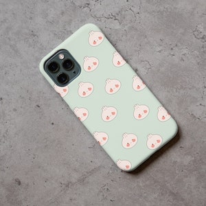 Peut inclure: Une coque de t&eacute;l&eacute;phone vert clair avec un motif r&eacute;p&eacute;t&eacute; de petits pains blancs en dessin anim&eacute; avec des joues roses. La coque a un objectif d'appareil photo noir.
