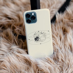 Peut inclure: Une coque de t&eacute;l&eacute;phone blanche avec une illustration en noir et blanc d'un chat tenant une plan&egrave;te. Le chat est entour&eacute; d'&eacute;toiles et de cercles.
