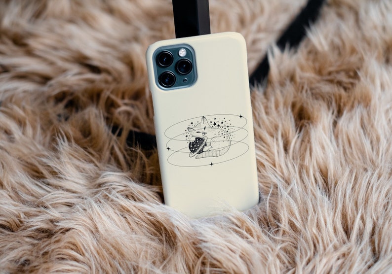 Peut inclure: Une coque de t&eacute;l&eacute;phone blanche avec une illustration en noir et blanc d'un chat tenant une plan&egrave;te. Le chat est entour&eacute; d'&eacute;toiles et de cercles.