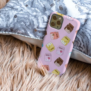 Peut inclure: Une coque de t&eacute;l&eacute;phone rose avec un motif de cartons de lait dessin&eacute;s anim&eacute;s avec diff&eacute;rentes garnitures de fruits et de chocolat. Les cartons de lait portent l'inscription "Lait".
