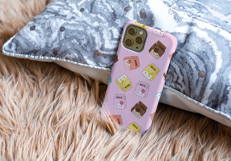 Peut inclure: Une coque de t&eacute;l&eacute;phone rose avec un motif de cartons de lait dessin&eacute;s anim&eacute;s avec diff&eacute;rentes garnitures de fruits et de chocolat. Les cartons de lait portent l'inscription "Lait".