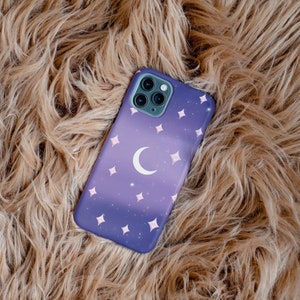 Peut inclure: Une coque de t&eacute;l&eacute;phone violette avec une lune croissante et des &eacute;toiles blanches sur un fond brun moelleux.