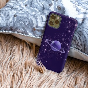 Peut inclure: Une coque de t&eacute;l&eacute;phone violette avec un motif de galaxie repr&eacute;sentant une plan&egrave;te avec des anneaux et des &eacute;toiles scintillantes.
