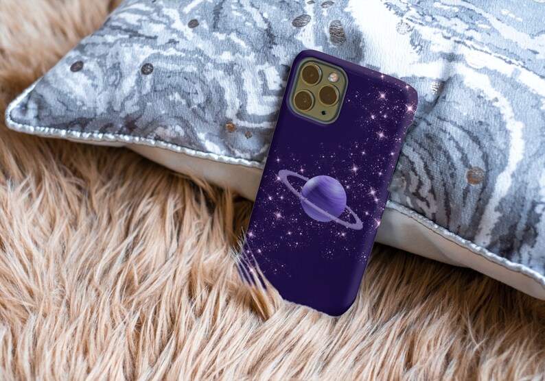 Peut inclure: Une coque de t&eacute;l&eacute;phone violette avec un motif de galaxie repr&eacute;sentant une plan&egrave;te avec des anneaux et des &eacute;toiles scintillantes.