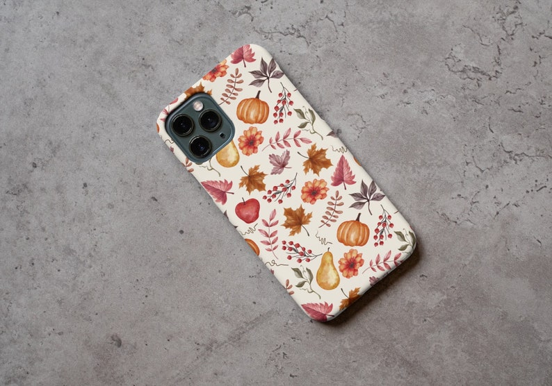 May include: A white iPhone case with a fall-themed design. The case features a pattern of red, orange, and yellow leaves, pumpkins, and pears.