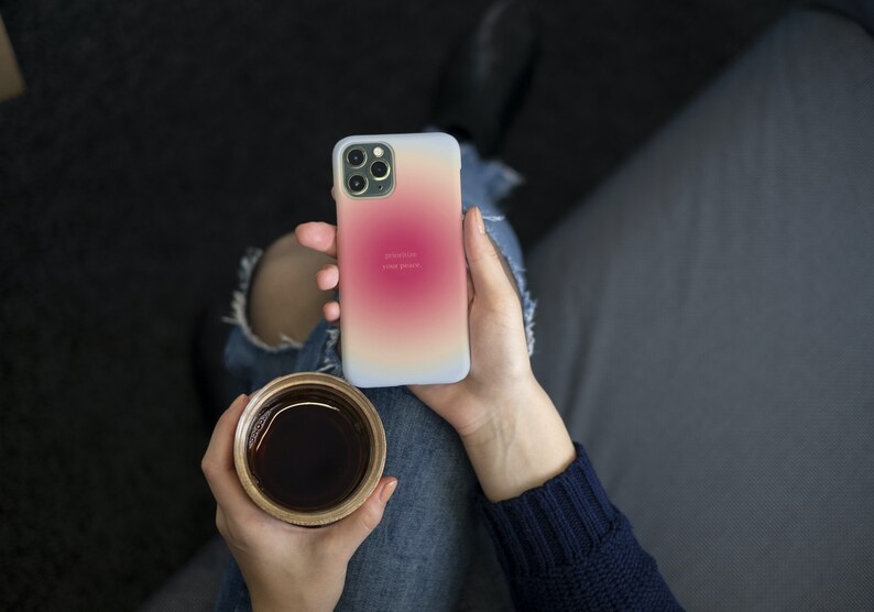 Pu&ograve; includere: Una persona tiene in mano una custodia per iPhone bianca con un gradiente di rosa, arancione e giallo. La custodia ha il testo "positivit&agrave;" e "il tuo potere" stampato su di essa. La persona tiene anche una tazza di caff&egrave;.