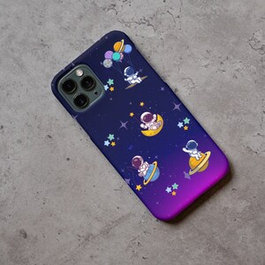 Peut inclure: Une coque de t&eacute;l&eacute;phone de couleur violette et bleue sur le th&egrave;me de l'espace. Elle pr&eacute;sente un fond de galaxie avec des &eacute;toiles et des plan&egrave;tes, et quatre astronautes flottant dans l'espace.