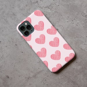 May include: A white phone case with a pink and white pattern of hearts. The case has a camera lens cutout and a cutout for the phone's buttons.