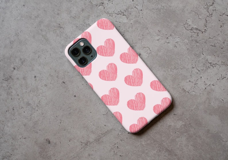 May include: A white phone case with a pink and white pattern of hearts. The case has a camera lens cutout and a cutout for the phone's buttons.