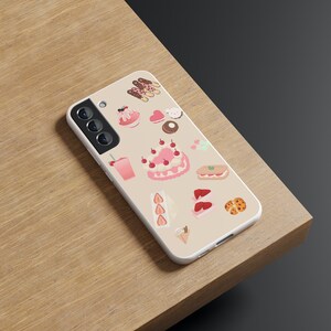 Peut inclure: Une coque de t&eacute;l&eacute;phone blanche avec une vari&eacute;t&eacute; d'autocollants de desserts roses et bruns, notamment des g&acirc;teaux, des biscuits et des glaces.