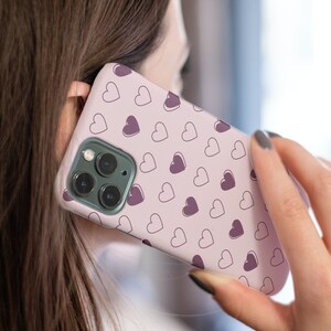 May include: A pink phone case with a pattern of small hearts in shades of pink and purple.
