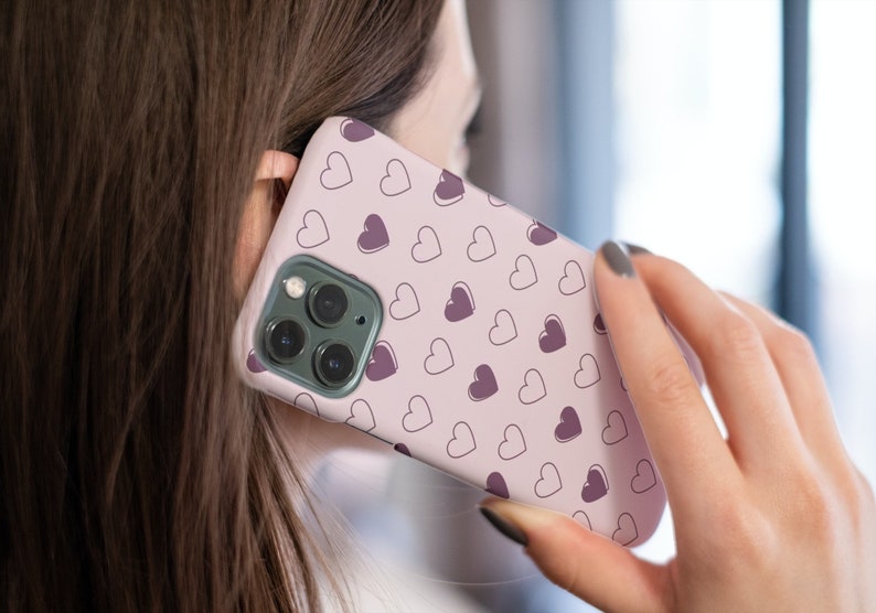 May include: A pink phone case with a pattern of small hearts in shades of pink and purple.