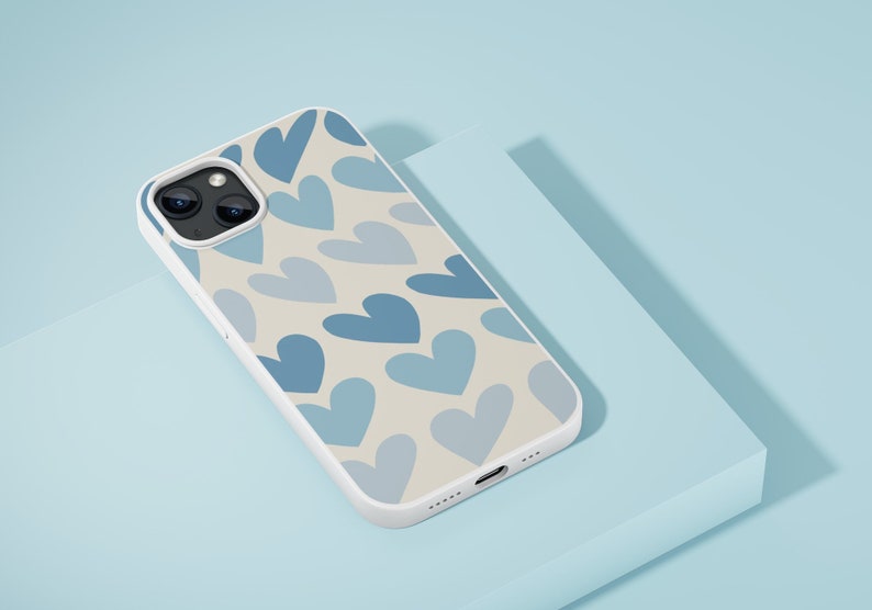 May include: A white phone case with a pattern of blue hearts on a cream background. The case has a camera lens cutout and a charging port.