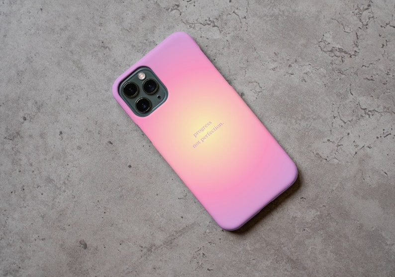 Pu&ograve; includere: Una custodia per telefono con sfumatura rosa e gialla con una scritta bianca che recita "progress not perfection".