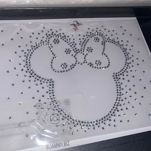 May include: A white background with a clear sheet of adhesive-backed rhinestones in the shape of a cartoon character. The character is a simple outline of a bear with two ears and a round body. The rhinestones are clear and sparkle. The text "@JAMMY.BIZ" is at the bottom of the image.