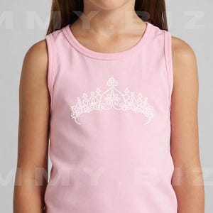 Könnte beinhalten: Ein hellrosa ärmelloses Tanktop mit einer mittigen Grafik einer Tiara aus kleinen weißen Strasssteinen. Das Design befindet sich im Brustbereich des Kleidungsstücks, das einen Rundhalsausschnitt und eine schlichte, klare Form hat.