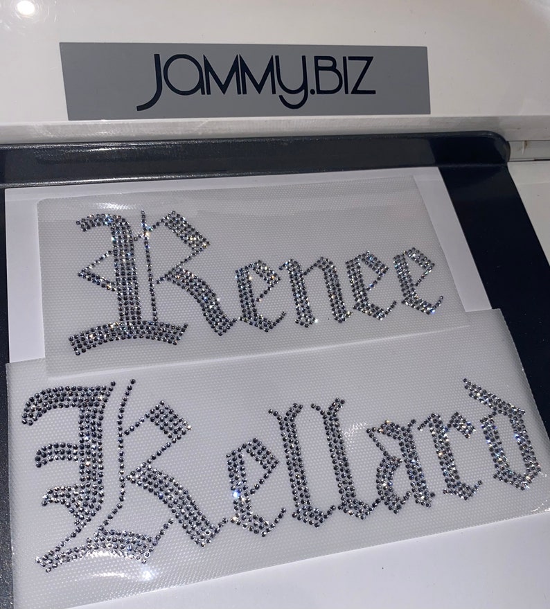 Puede incluir: Dos transferencias de diamantes de imitaci&oacute;n termoadhesivos sobre l&aacute;minas adhesivas transparentes. La l&aacute;mina superior muestra el nombre Renee y la inferior el nombre Kellard, ambos en fuente g&oacute;tica. El texto JAMMY.BIZ es visible arriba.