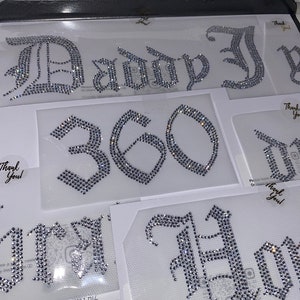 Puede incluir: M&uacute;ltiples transferencias de diamantes de imitaci&oacute;n para planchar con cristales de color plateado dispuestos en letras y n&uacute;meros de estilo g&oacute;tico. Los dise&ntilde;os incluyen el texto "Daddy", el n&uacute;mero "360" y otras palabras parciales en l&aacute;minas adhesivas transparentes con etiquetas "Thank You".