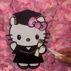 Puede incluir: Un personaje de Hello Kitty blanco y negro con una toga y un gorro de graduación negros, sosteniendo un rollo. El personaje tiene un lazo rosa y detalles de purpurina. El fondo es una pared de flores rosas.