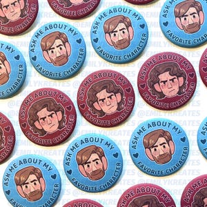 May include: A collection of round buttons in shades of blue and burgundy. Each button features a cartoon illustration of a character's face, with the text "ASK ME ABOUT MY FAVORITE CHARACTER" encircling the image.