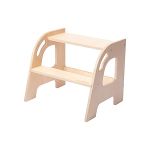 Puede incluir: Un taburete de madera natural con dos peldaños y bordes redondeados. El taburete tiene un recorte en el lateral para un agarre fácil.