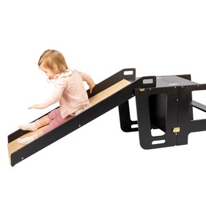 Joyful toddler sliding down from a Kitchen Tower attachment. Learning Tower fun in action.