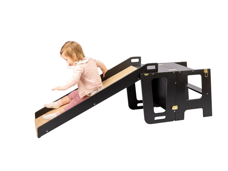 Joyful toddler sliding down from a Kitchen Tower attachment. Learning Tower fun in action.