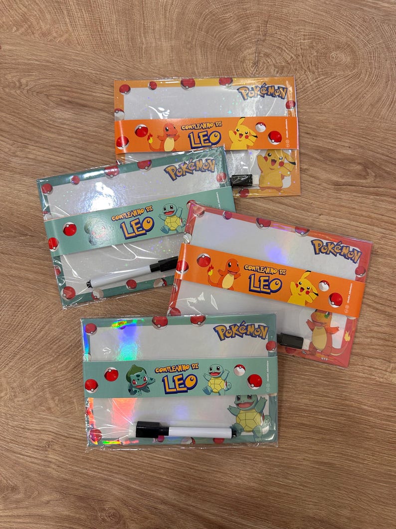 Puede incluir: Cuatro pizarras blancas rectangulares con la marca Pok&eacute;mon e ilustraciones de personajes. Cada pizarra est&aacute; envuelta en una banda de papel con el texto 'COMPLEANNO DI LEO', Charmander, Pikachu, Squirtle o Bulbasaur, e incluye un marcador borrable.