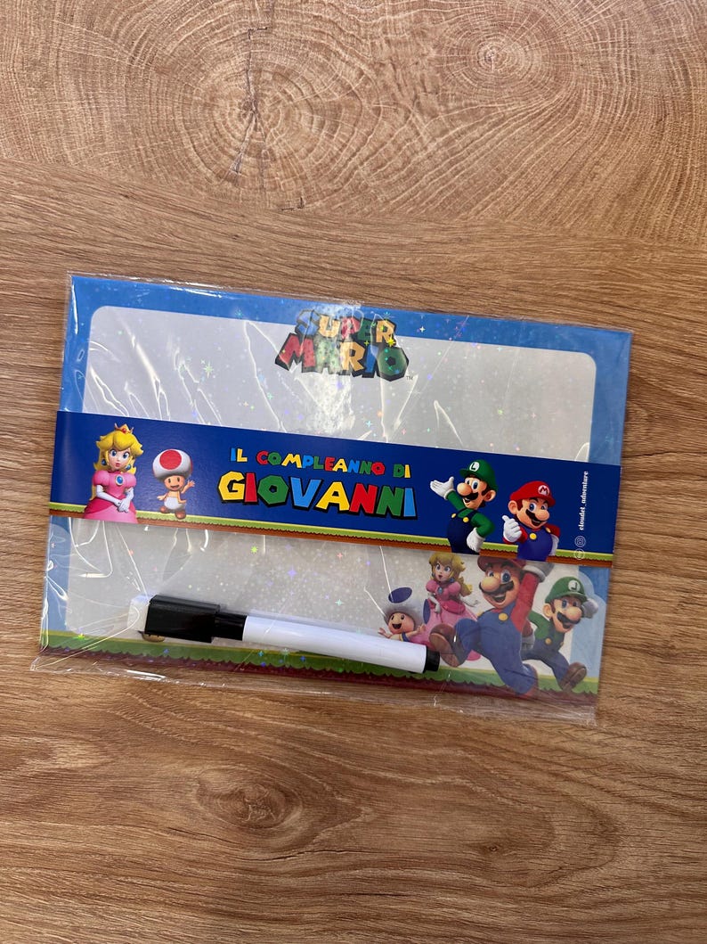 Puede incluir: Una pizarra blanca de borrado en seco con tem&aacute;tica de Super Mario en un envoltorio de pl&aacute;stico transparente. La pizarra muestra a la Princesa Peach, Toad, Mario y Luigi, con el texto "IL COMPLEANNO DI GIOVANNI" impreso en el centro. Incluye un rotulador negro.