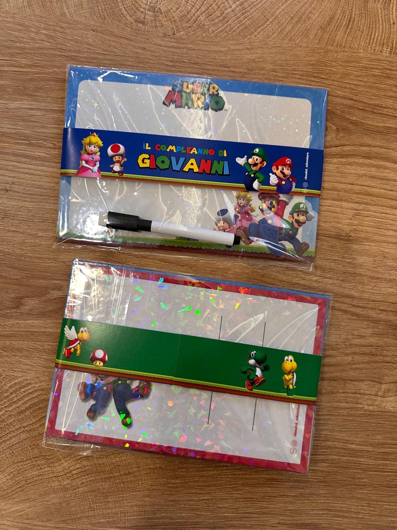 Puede incluir: Dos pizarras blancas rectangulares con tem&aacute;tica de Super Mario en envoltorio de pl&aacute;stico transparente. La superior muestra a la Princesa Peach, Toad, Luigi y Mario con el texto IL COMPLEANNO DI GIOVANNI y un rotulador negro. La inferior muestra a Yoshi y Koopa.