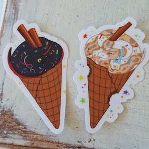 May include: Two stickers depicting snakes in ice cream cones. One shows a black snake with sprinkles and cinnamon sticks, the other a tan snake with a blue bow tie. Both are in brown waffle cones with colourful star accents.