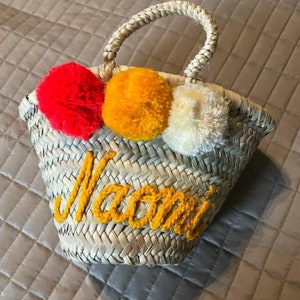 Op de afbeelding: Een strooien tas met het woord "Mami" geborduurd in geel en drie pompoenen in rood, oranje en wit.