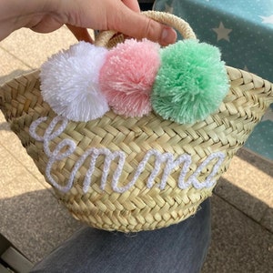 Op de afbeelding: Een kleine strooien tas met een witte geborduurde naam "Emma" en drie pompoenen in wit, roze en groen.