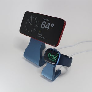 Op de afbeelding: Een blauwe oplaadstandaard met twee witte oplaadkabels. Een rode iPhone staat op de standaard en toont de tijd en het weer in Austin, Texas. De temperatuur is 64 graden. Een blauwe Apple Watch staat op de andere standaard en toont de tijd en de dag van de week. Het horloge heeft een groene wijzerplaat.